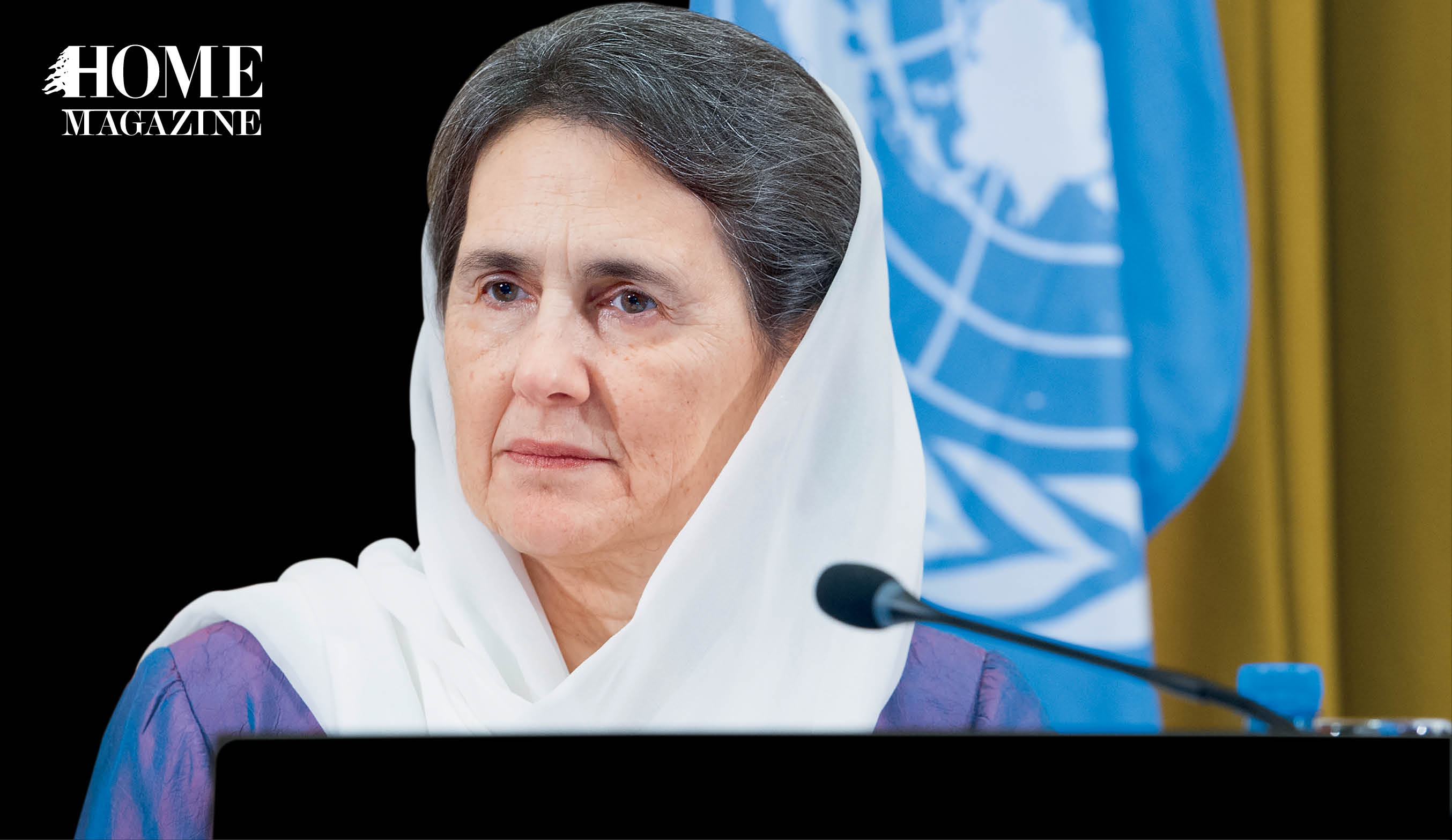 Old woman with white veil on her greyish hair with microphone in front of her and a blue flag behind her